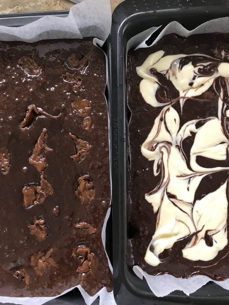 Two baking trays with brownie mixture. The one on the left hand side has salted caramel, the one on the right hand side is cheesecake