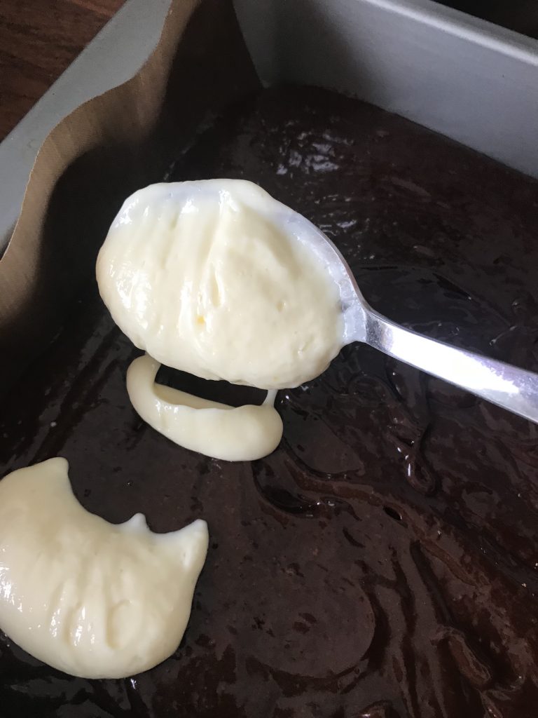 a table spoon dolloping cheesecake mixture into the brownie mix