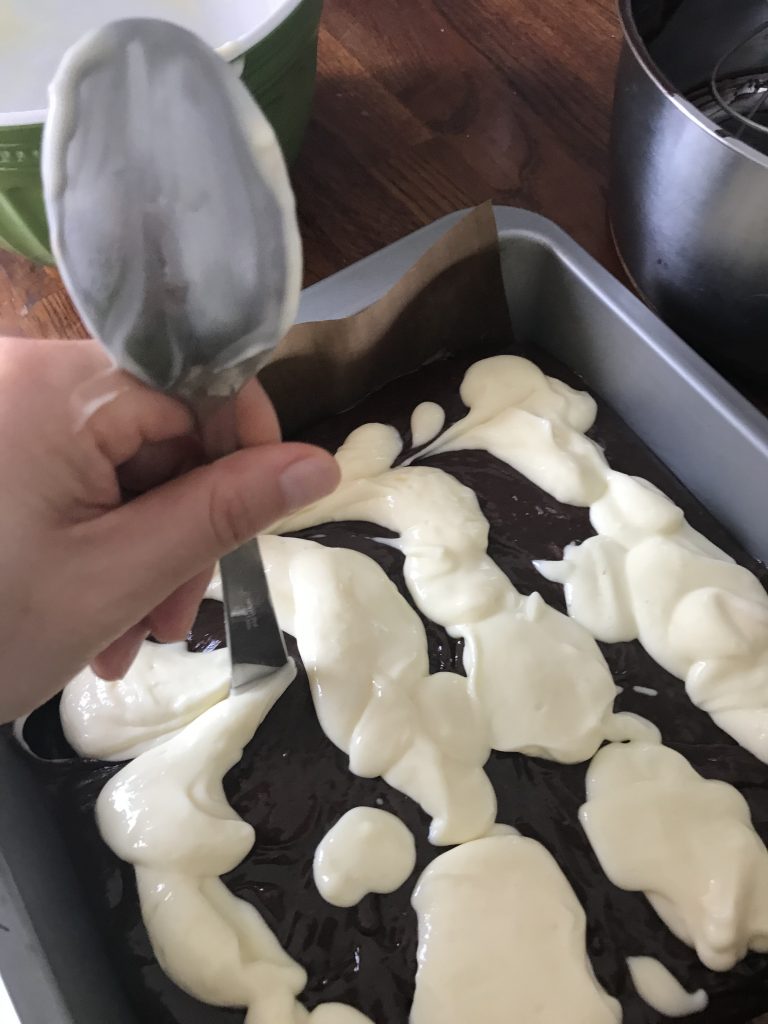 the end of the spoon going up and down to create a swirling effect between the brownies and the cheesecake mixtures